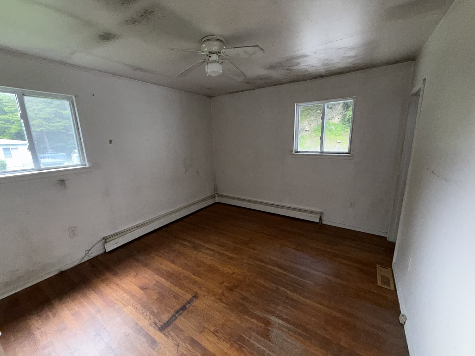 Empty room with wood flooring, two windows and a ceiling fan