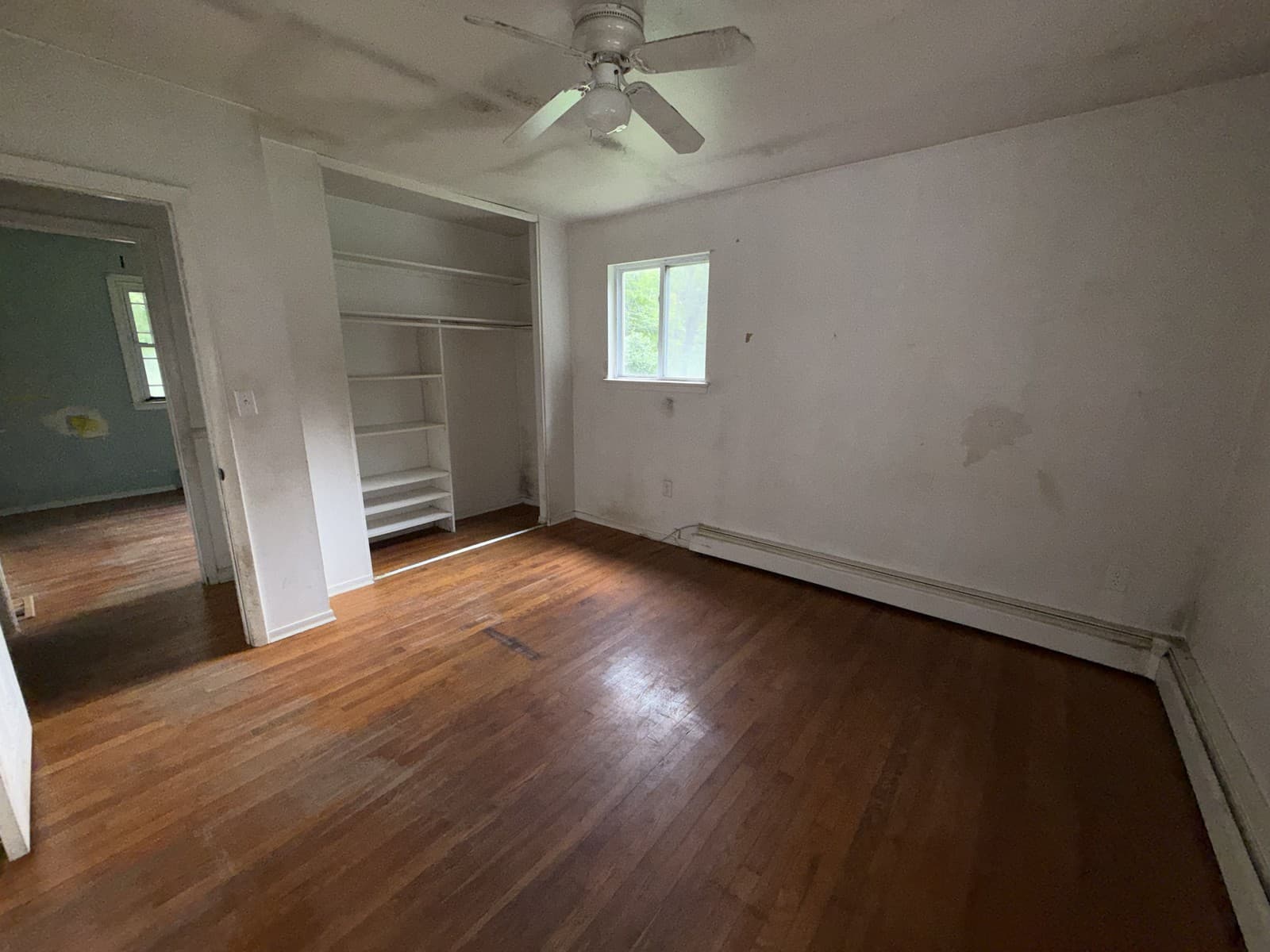 Empty room with wood flooring, a window, ceiling fan and open closet